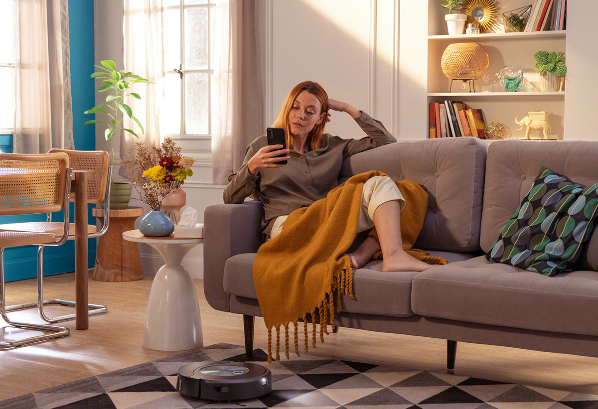 απεικονίζεται η σκούπα σε ένα σαλόνι και πάνω στον καναπέ μία γυναίκα που διαβάζει ένα βιβλίο
